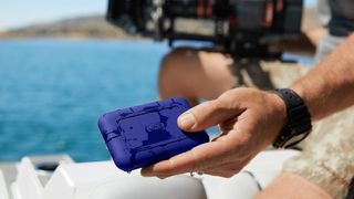 The LaCie Rugged SSD Pro5 held in a person&#039;s hands near a camera and water