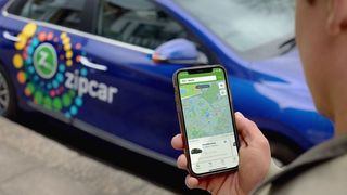 A Zipcar car and a person holding their phone with the Zipcar app open