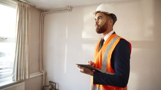 Surveyor in hi-vis jacket with tablet in room of house needing updating