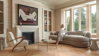 Large formal sitting room with neutral walls and Scandi-inspired furniture, Art Deco fireplace with artwork above, herringbone wood flooring and a large period window