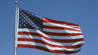 The flag of the United States fluttering in the wind against a blue sky background.