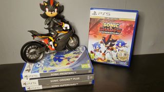 Image of a pile of Sonic PS5 games, including Sonic X Shadow Generations on a black shelf with a Shadow figure on a bike form the Sonic 3 movie sitting on top of the pile taken by author Rosalie Newcombe.