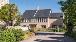 A wide angle shot of a self build with light stone with a row of windows on a sunny day