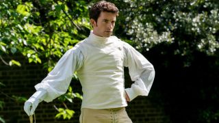 Anthony Bridgerton in fencing gear, holding sword in his left hand and putting his right hand on his hip.