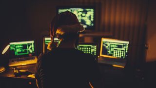 A hacker in a Christmas hat in front of multiple screens 