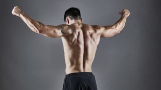 Male with back to camera and arms raised against grey backdrop