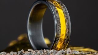 a black metal ring with a golden center inset bordered by crushed rock.