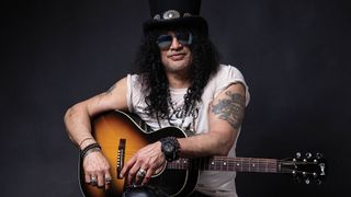 Slash wears a top hat and holds a GIbson J-45 acoustic guitar