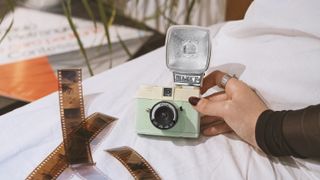 The Lomography Half-Frame Lomourette held by a person on a blanket with film strips