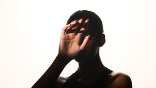 A photo of a model masked in shadow with her hand stylistically lit, highlighting the Ultrahuman Rare Desert Rose smart ring on her index finger.