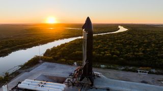 a black bellied chrome spaceship stands on a concrete pad with a winding creek giving way to a sunset in the distance.