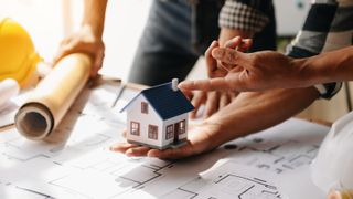 hands holding model house over architect plans