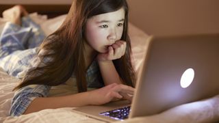 A child lying in bed on their laptop