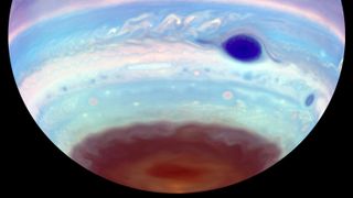 The southern hemisphere of Jupiter hangs from above in black space, striped in false color blues, violets, and dark reds