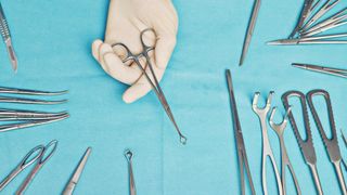 a surgeon&#039;s gloved hand holds a tool over a table of surgical tools