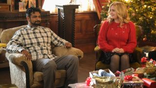 Pictured (L-R): Utkarsh Ambudkar as Jay sitting in an armchair and Rose McIver as Samantha sitting next to him smiling.