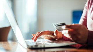 A side-on shot of someone&#039;s hands using a laptop and holding a credit card, to represent online payment technology and online banking.