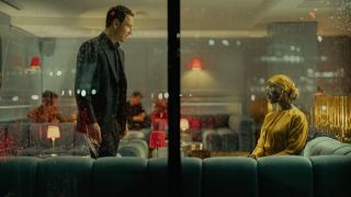 Undercover agent Martian (Michael Fassbender) and Sami Zahir (Jodie Turner-Smith) seen through the window of a hotel lobby at night in spy thriller The Agency.