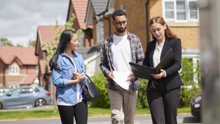 Young couple with estate agent outside modern houses