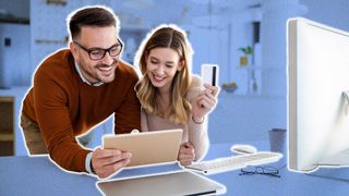 Couple leaning over desk looking at a tablet. The woman is holding a credit card in her left hand.