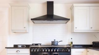 black cooker hood above range oven in kitchen with cream shaker units