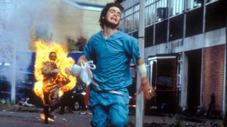 Jim runs away from a zombie on fire chasing after him in 28 Days Later.