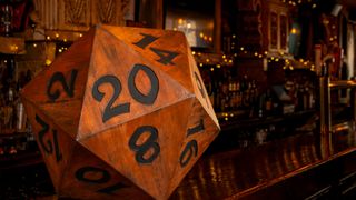 A giant wooden d20 on a wooden bar surface, with twinkling fairy lights in the background