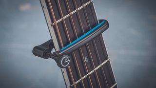 Closeup of a black G7th capo on the neck of an acoustic guitar