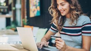 A smiling young woman is holding a credit card and typing on a laptop