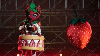 Strawberry Shortcake singing next to a wrecking ball on The Masked Singer stage