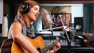 Woman records vocals and guitar in a studio