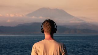 Rear view of man with headphones against Bali island at sunset. 