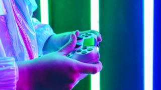 A pair of hands holding a white controller in a dark room with colorful neon lights in the background