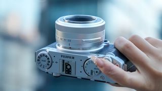 The white TTArtisan 27mm f/2.8 lens mounted on a Fujifilm camera held in a person&#039;s hand