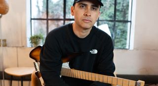 Rodrigo Gouveia wears a black ballcap and is seated with his headless Strandberg Boden 6 in sunburst