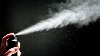 Person spraying a deodorant can with black background