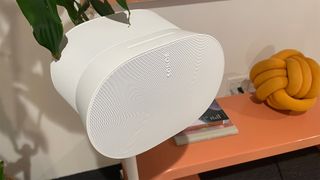 A white Sonos Era 300 speaker on its stand next to a wooden countertop.