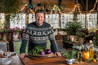 Jamie Oliver in his Christmas jumper and festively redecorated kitchen with a big bowl of green veg.