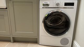 A white Siemens heat pump tumble dryer in a utility room with grey cupboards