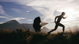 A young male sprints through the Scottish Highlands using a speed chute for extra resistance and increased power training. The sun sets and creates a beautiful silhouette of him running