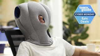 A man wearing a grey over-the-head ostrichpillow while sat at desk representing weird and wacky sleep tech