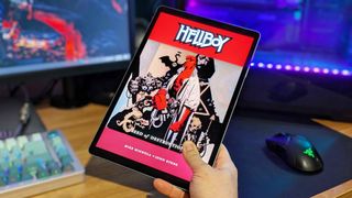 Samsung Galaxy Tab S10 Plus in-hand with a Hellboy comic cover on the screen in front of a computer desk.