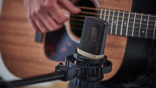 An acoustic guitar microphone with a man playing guitar in the background