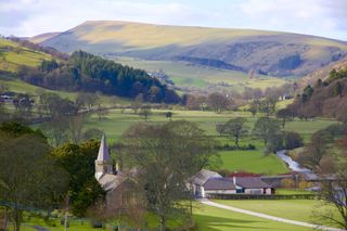 A view of rolling green hills with a small village and a church in a valley