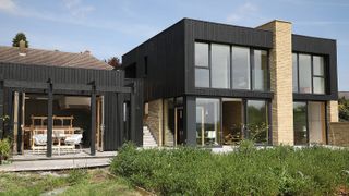 A self build home with small weaving studio built next to it clad in the same dark timber