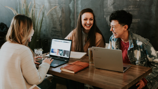 Three women with laptops sitting around a table laughing