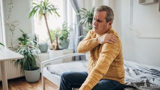 A man in yellow sweater rubs shoulder as he has shoulder pain