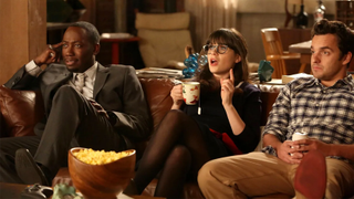 Characters of New Girl, Winston, Jess, and Nick sat on a brown leather couch reacting to what they&#039;re watching on TV, with a big bowl of popcorn