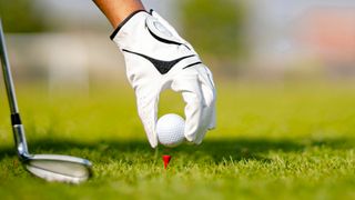 A golfer with the best golf gloves putting a ball on a tee