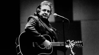 Johnny Cash performing on stage with his all-black guitar 